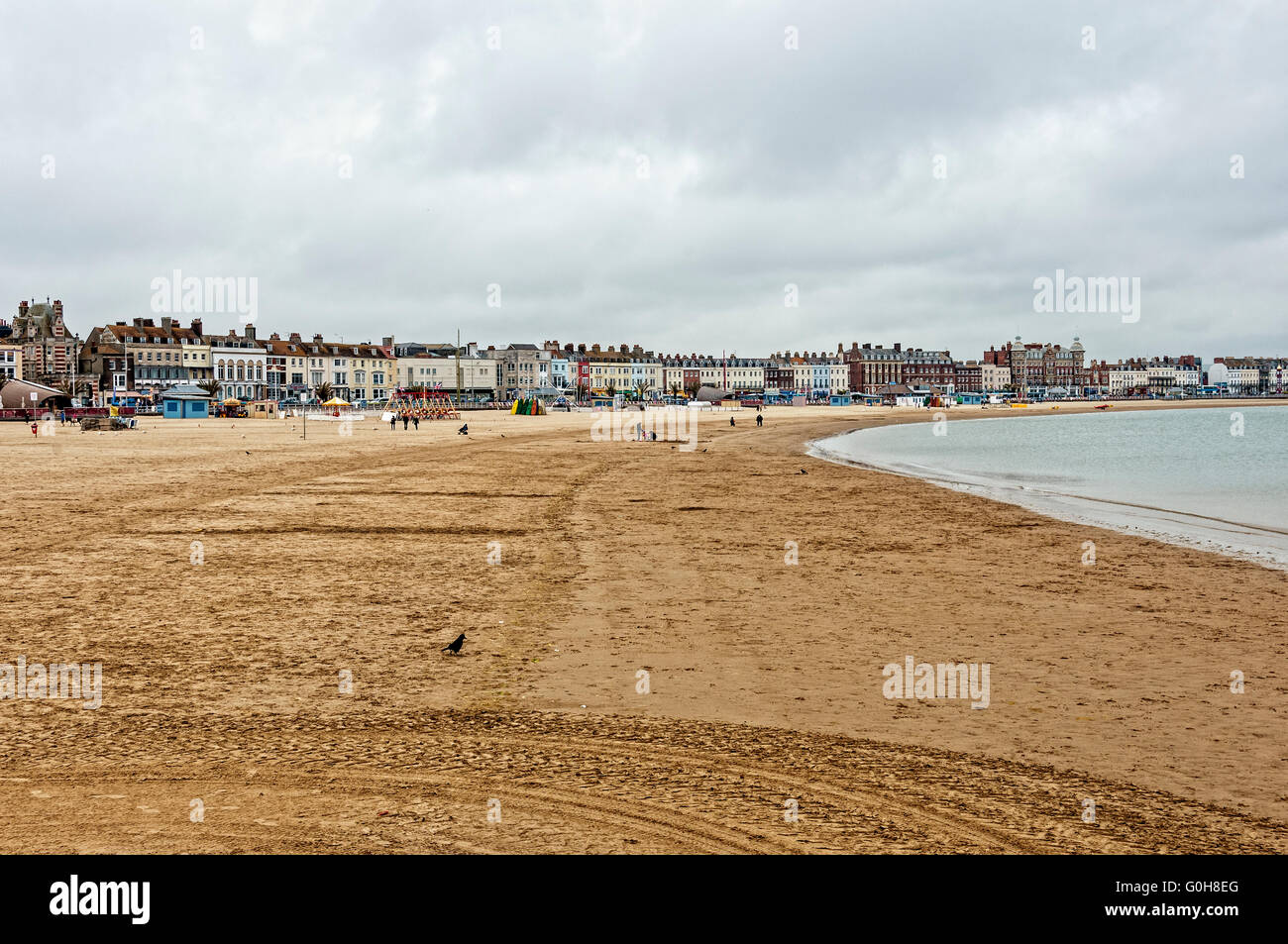 On a grey day the visitor attractions appear to remain unused on the nearly deserted Weymouth beach bordered by terraced houses Stock Photo