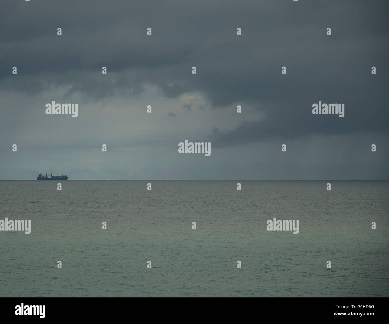 Container ship on horizon on calm grey green sea approaching stormy ...