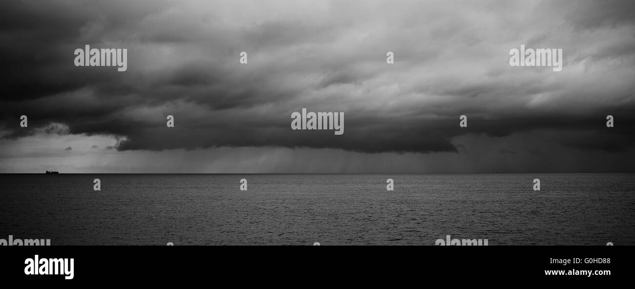 Large container ship on the horizon sailing toward very stormy clouds ...