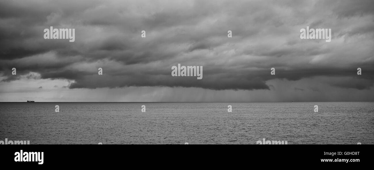 Large container ship on the horizon sailing toward very stormy clouds ...