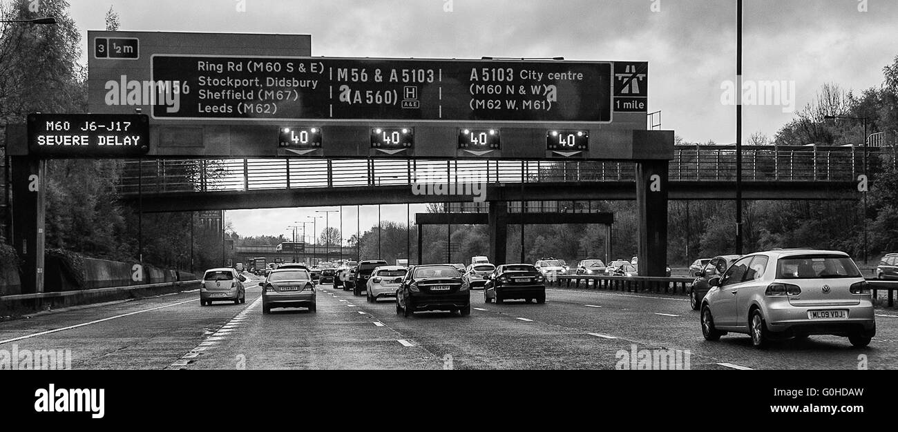 Motorway traffic queuing below overhead gantry with flashing matrix signs 40mph and severe delay warning Stock Photo