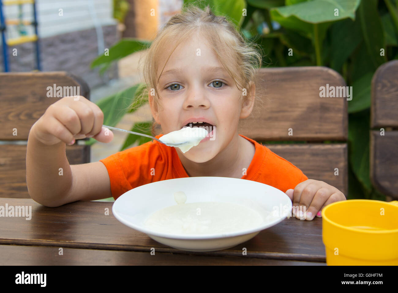 Funny five-year girl with pleasure eats porridge for breakfast Stock Photo