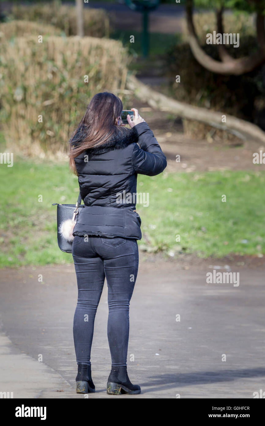 Woman with big buttocks in tight pants stands by the road with smartphone  in her hand on car background. Female fashion, car sharing, calling a taxi  concept Stock Photo