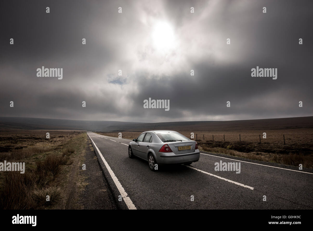 SIlver car on the Snake Pass road crossing the moors above Glossop in Derbyshire. Moody sky overhead. Stock Photo