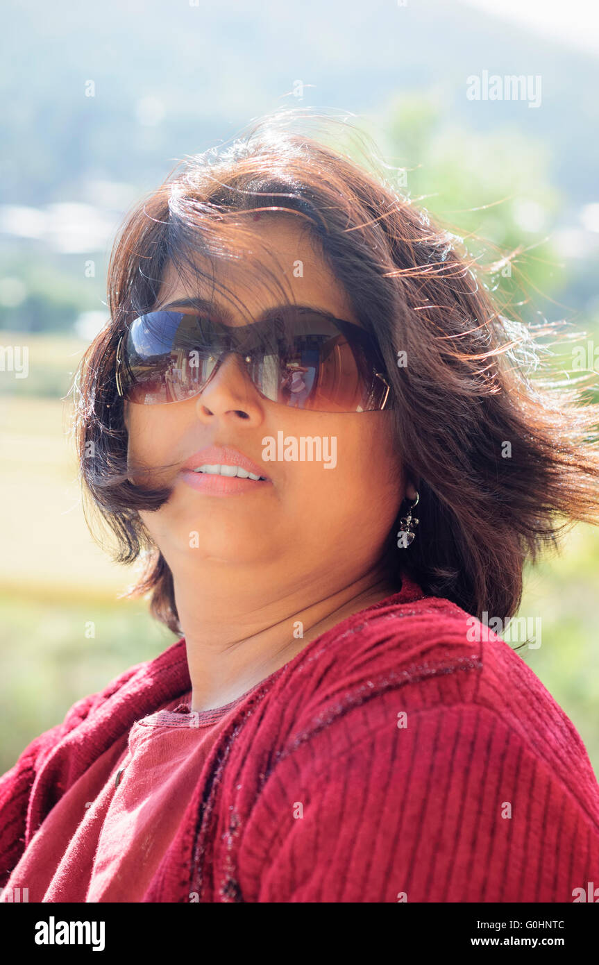 Portrait of a mature, Asian, Non-Caucasian, Bengali beautiful smiling lady with copy space wearing red dress and backlit Stock Photo