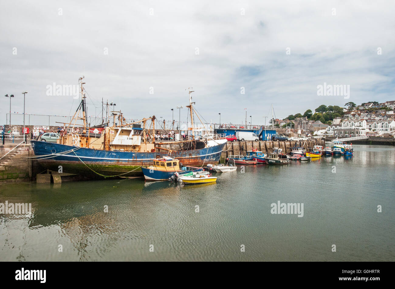 Brixham Harbour with people, boats, a large trawler all against the harbour wall, Devon Stock Photo