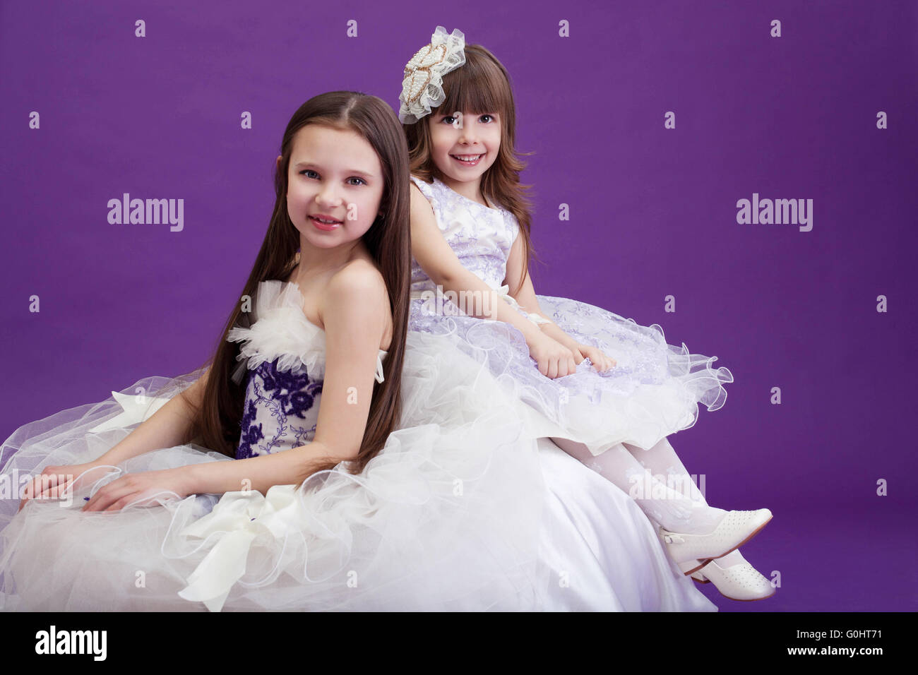 Two smiling little girls posing in elegant dresses Stock Photo - Alamy