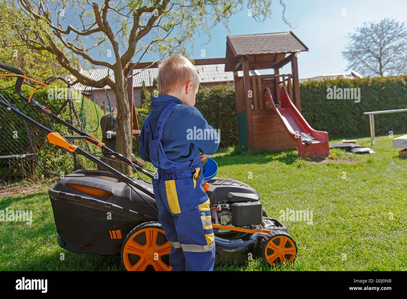 Cute, little boy mows the lawn. Boy inspects the mower, before driving or left engine oil Stock