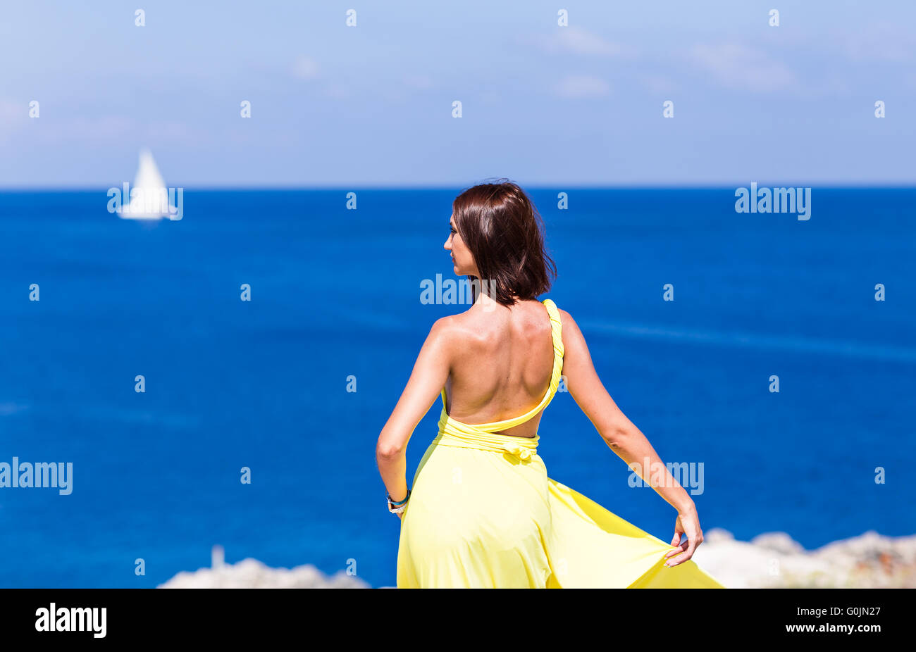 Young brunette woman in summer yellow dress standing on beach and ...
