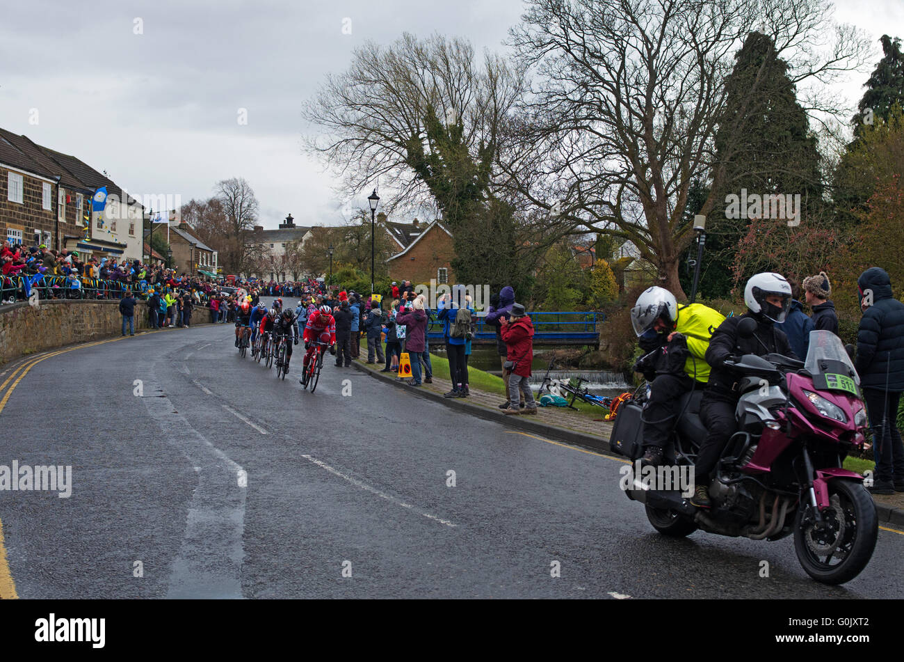 Great Ayton, North Yorkshire. 1 May 2016. In dull weather, crowds line the main street, as the leading cyclists in Stage 3 of the Tour de Yorkshire race through the village, preceded by the race motorcyclist. Stock Photo