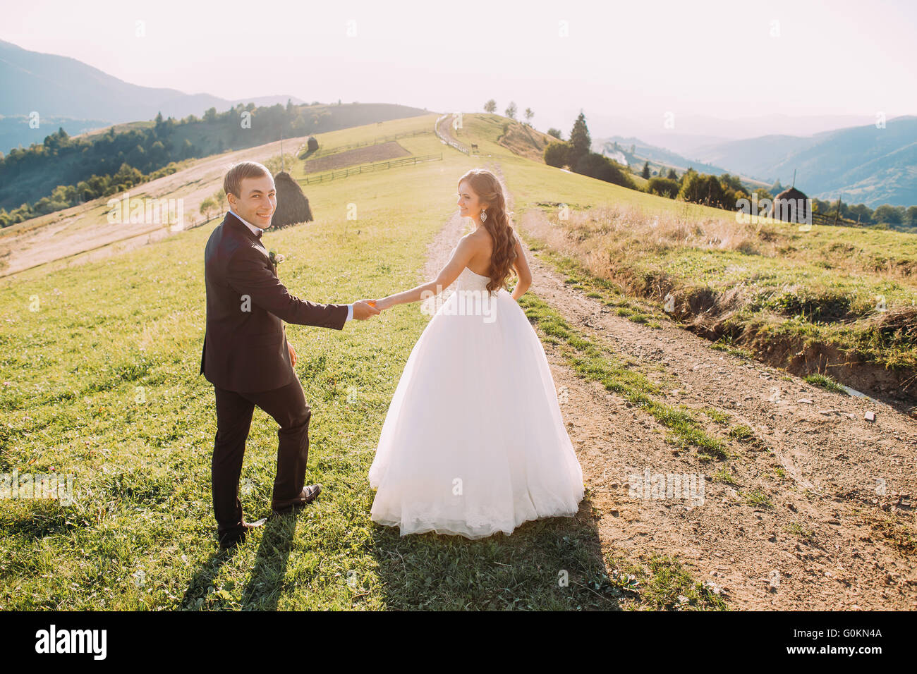Beautiful bride and groom walking back holding hands on meadow with ...