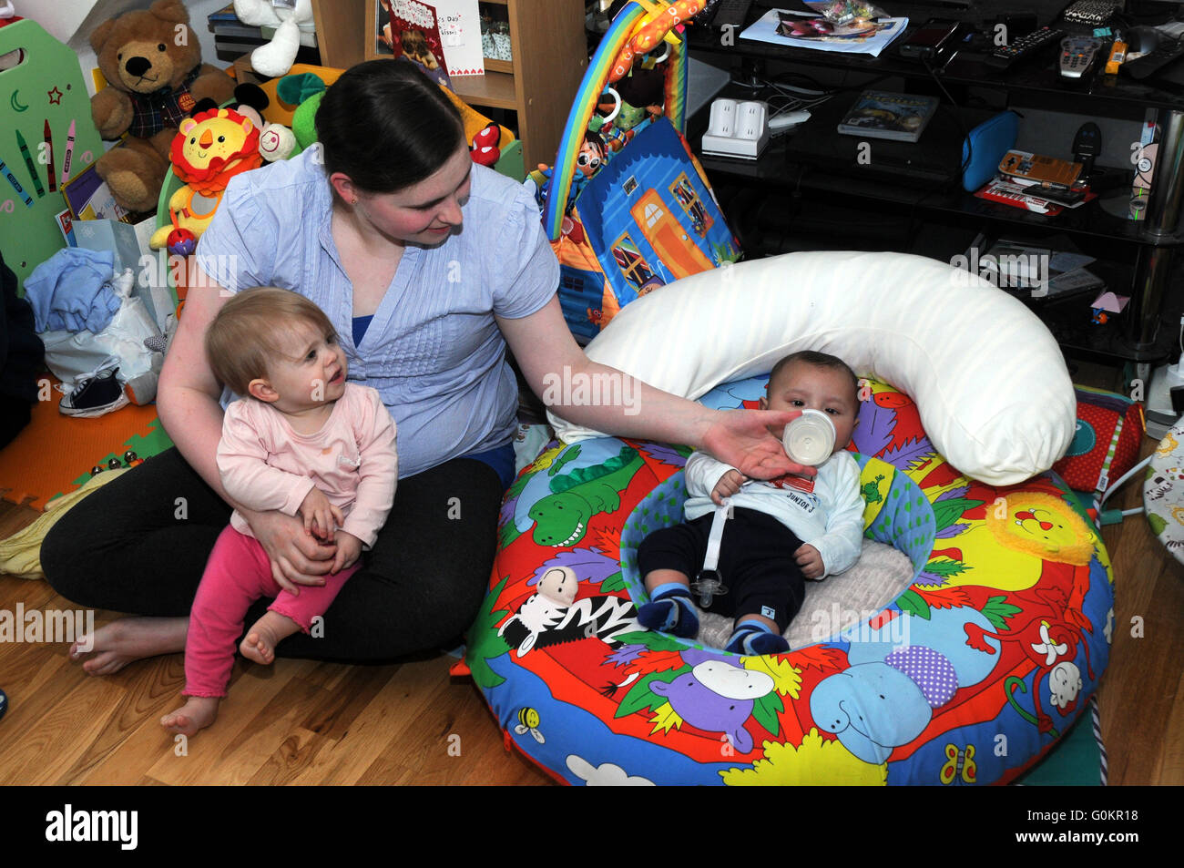 A young mum feeds her bay with a toddler looking on Stock Photo
