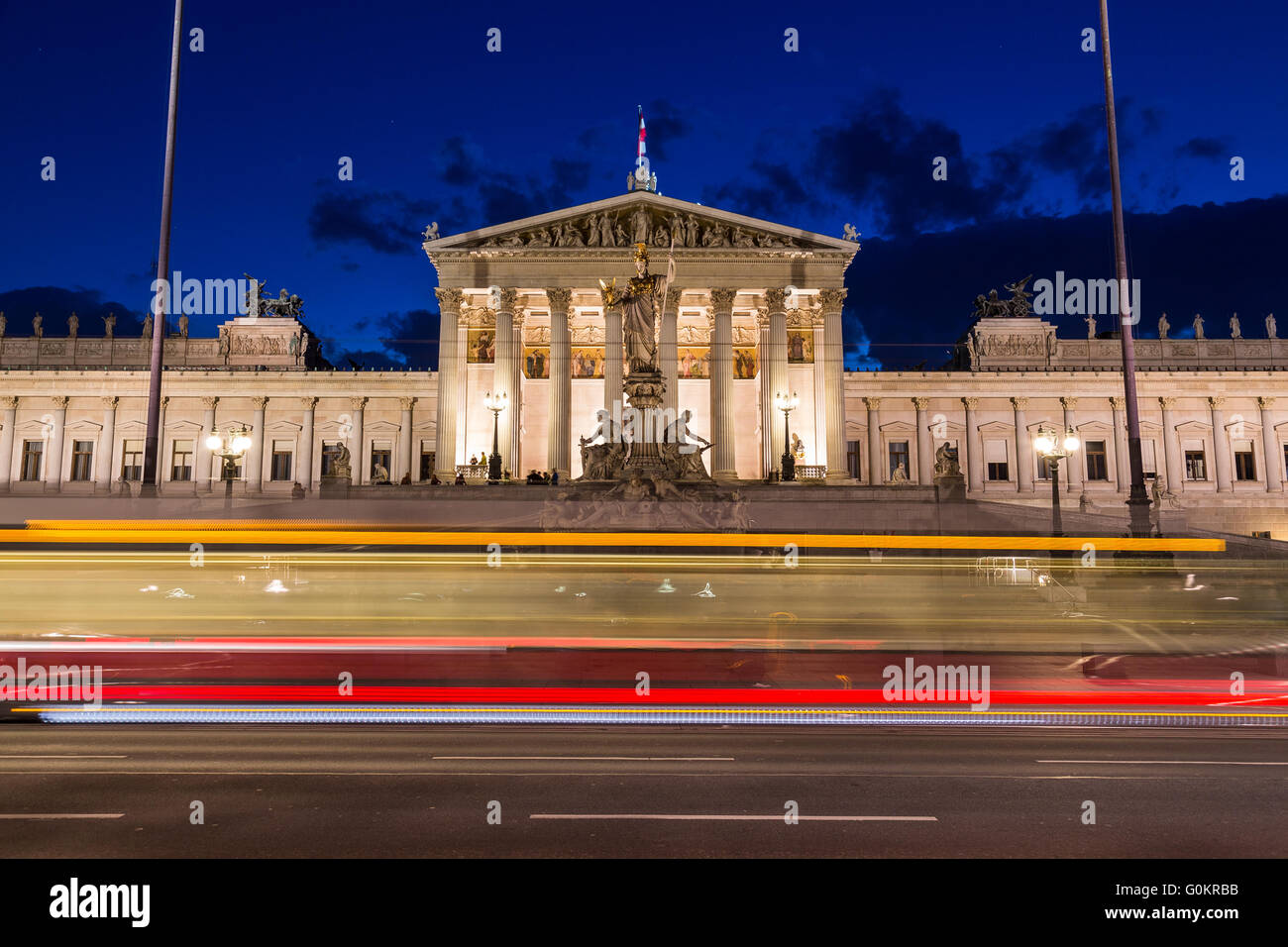 The outside of the Austrian Parliament building in Viennat at night. The blur of a tram can be seen going past in the foreground Stock Photo