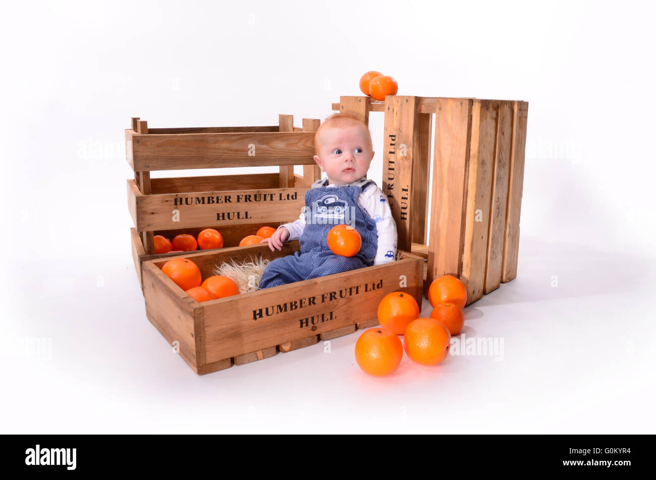 boy playing with oranges in market stall fruit boxes Stock Photo