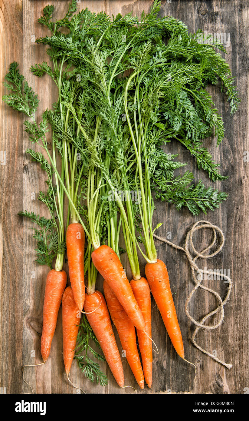 Karotte Roots Fresh carrot roots with green leaves over rustic wooden background ...