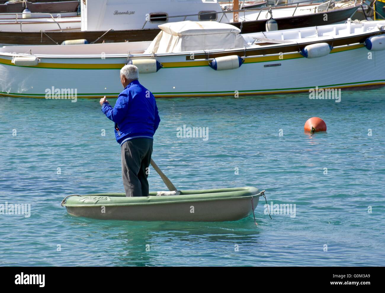 A man rowing a small boat across the bay to get his large boat Stock Photo