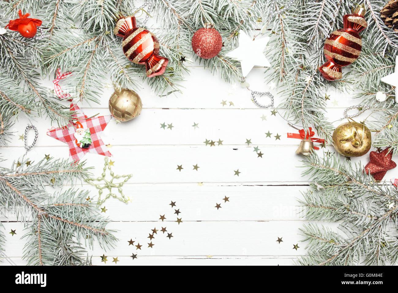 Christmas or New Year background: fur-tree branches, colorful glass balls, decoration and glittering stars on white wood, top view, copy space. Stock Photo