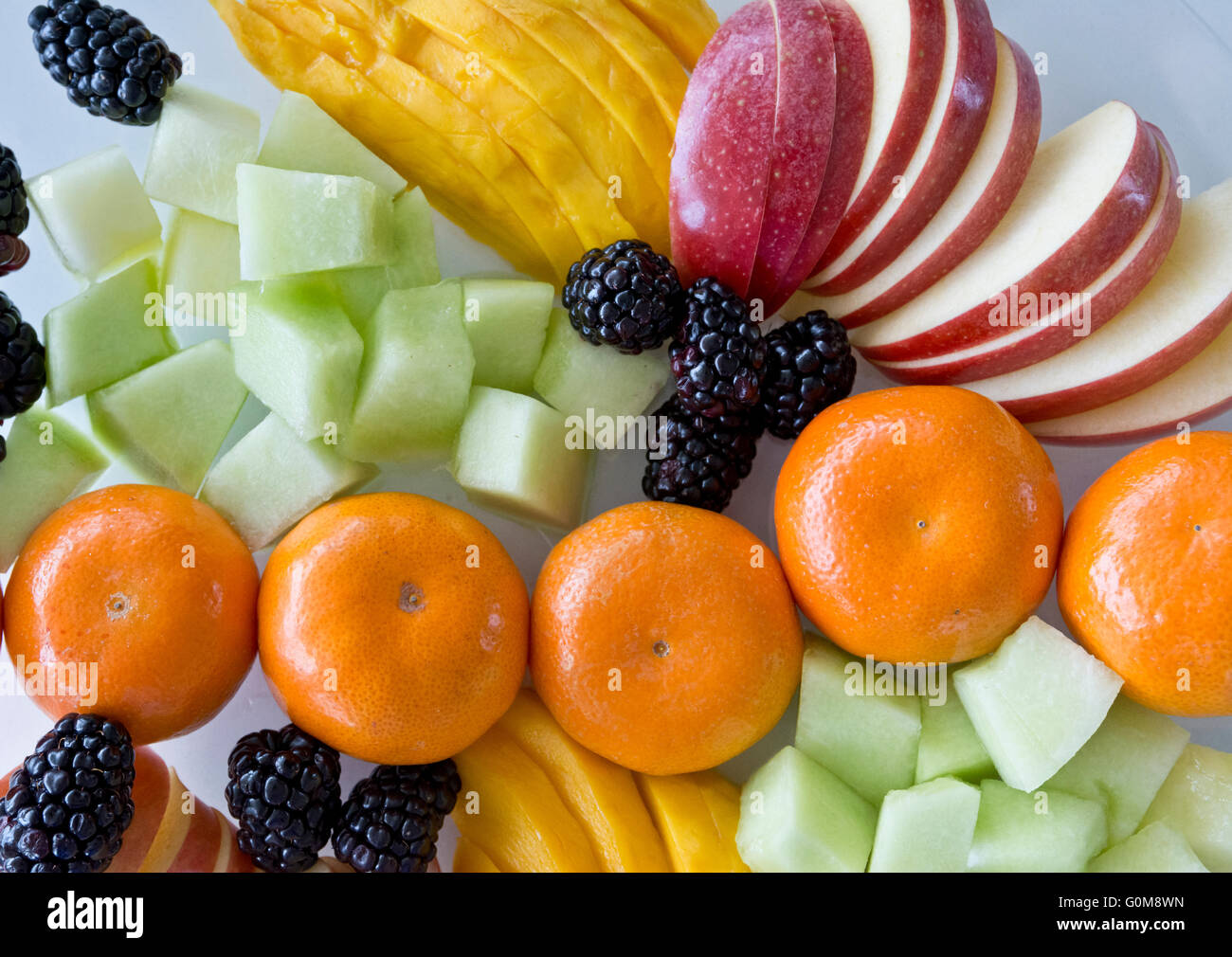 Colourful mixed fruit plate with sliced apples mangoes honeydew melon