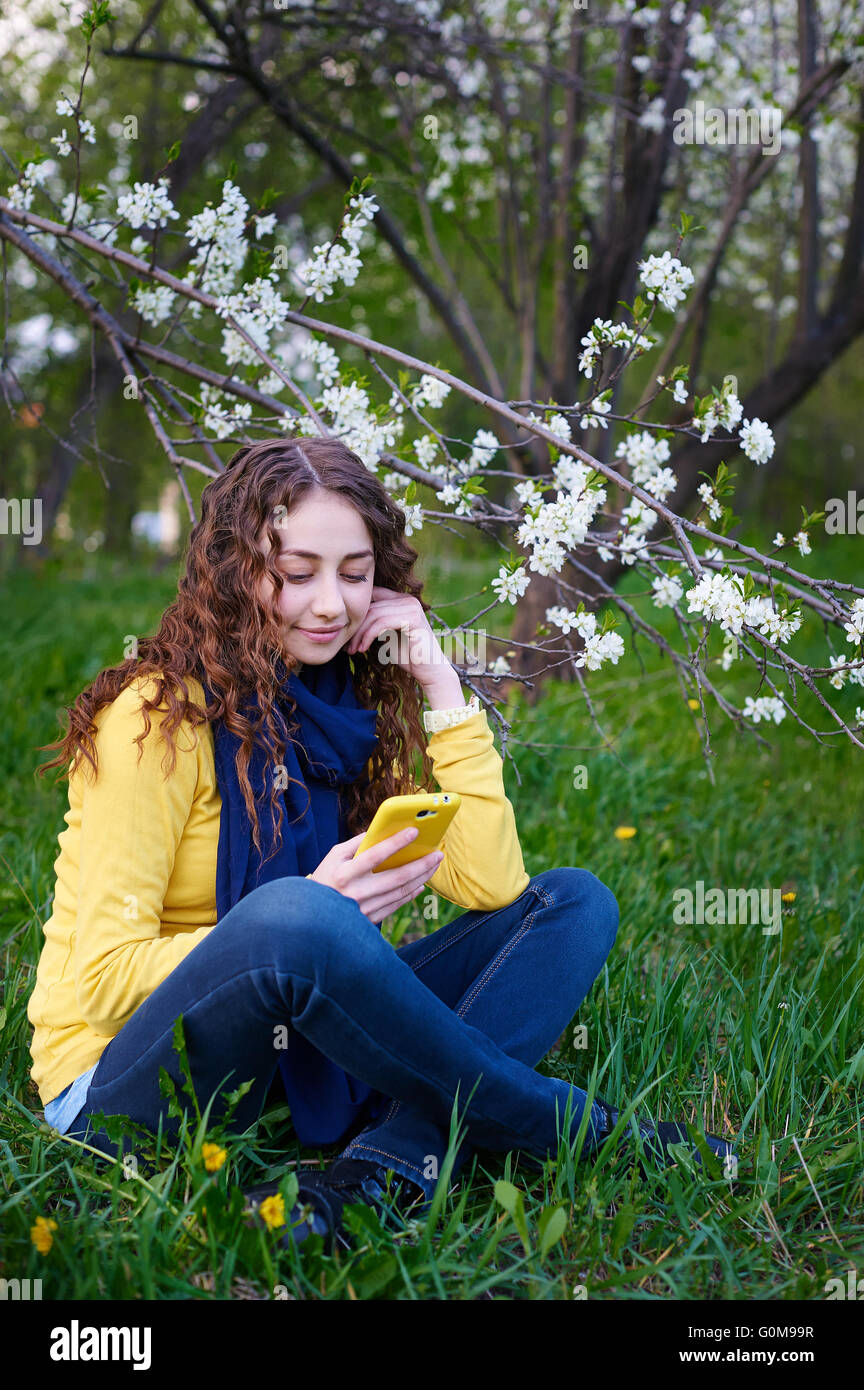 Beautiful young woman sitting on grass with a smartphone Stock Photo
