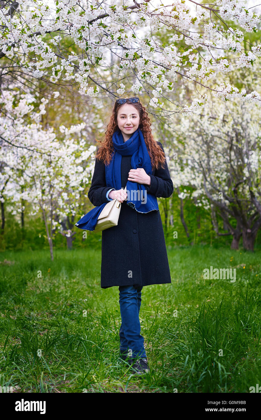young woman in coat walking at blossoming spring cherry garden Stock Photo