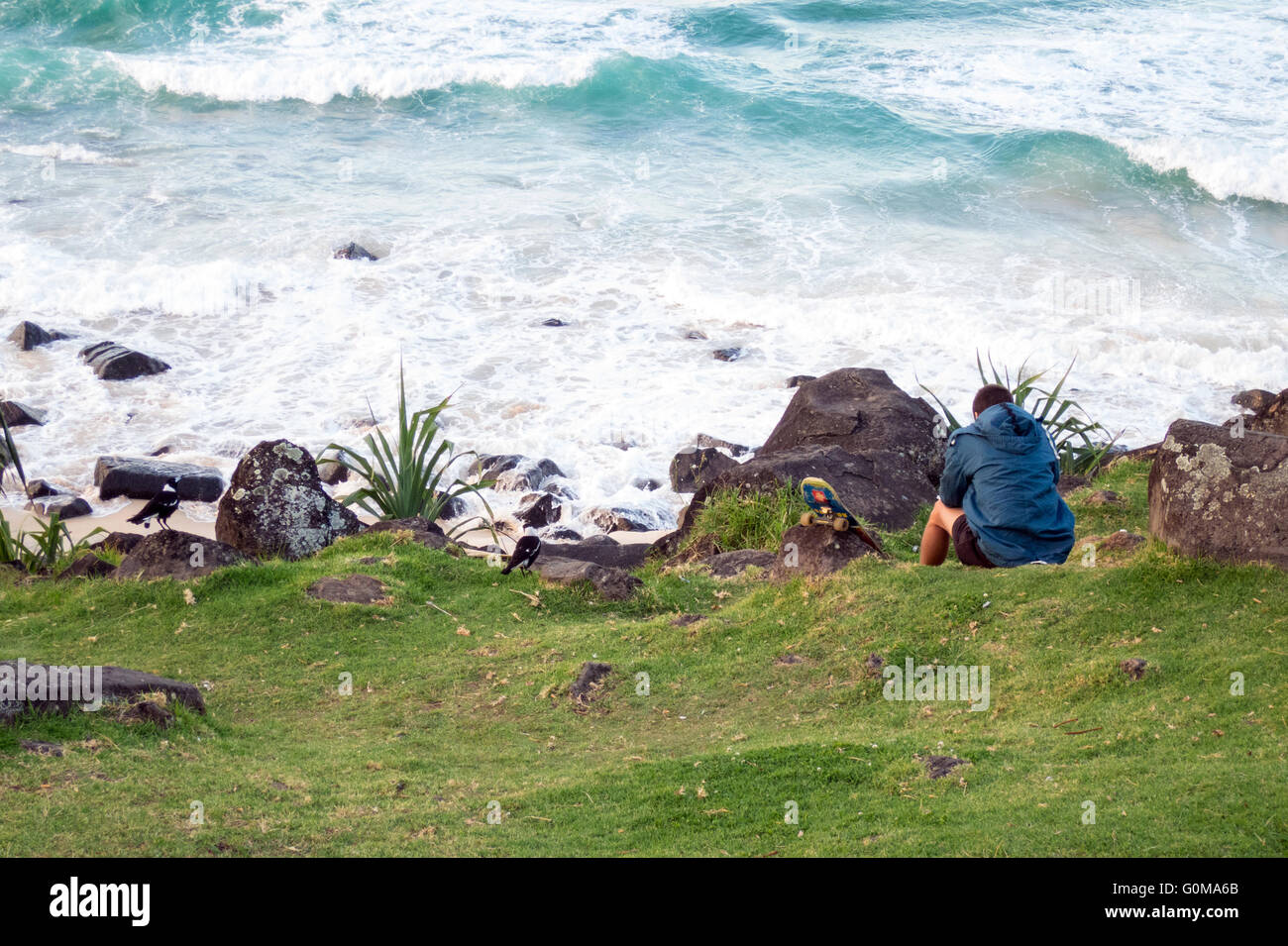 A young man sits looking at the Pacific Ocean at Burleigh Heads in Queensland Australia Stock Photo