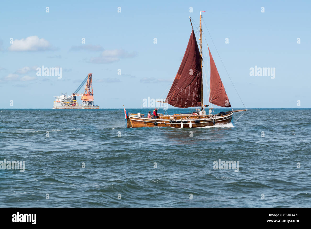 Small sailing yacht and big cargo ship crossing on North Sea near port