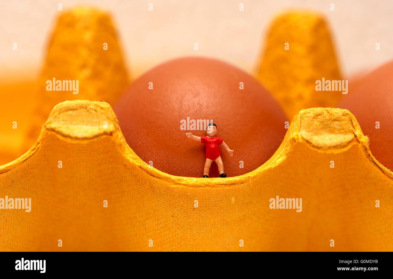 A miniature figurine toddler boy standing on an egg box in front of an egg Stock Photo