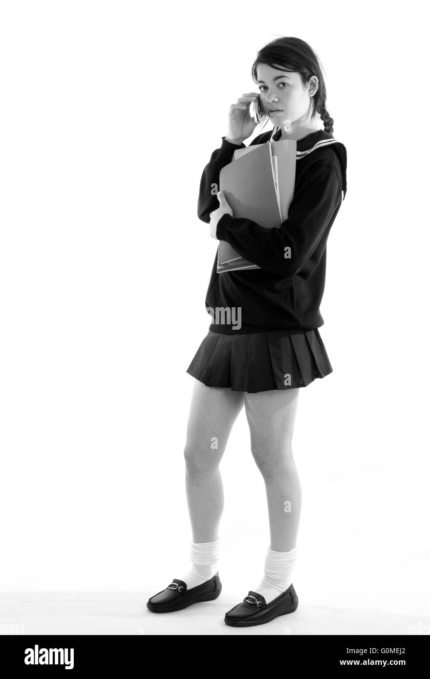 Mixed race young woman dressed in a Japanese style schoolgirls uniform with a very short skirt carrying books Stock Photo