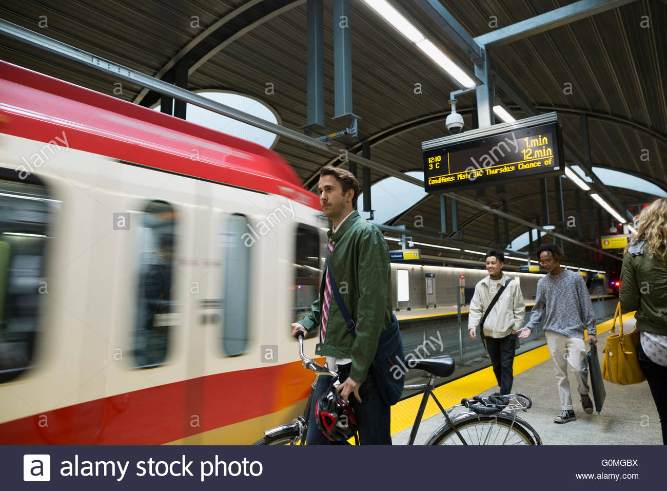 Businessman with bicycle watching arriving subway on platform Stock