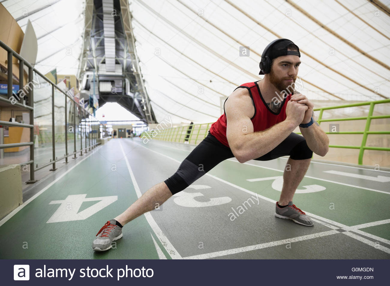 Runner doing side lunge stretch on indoor track Stock Photo