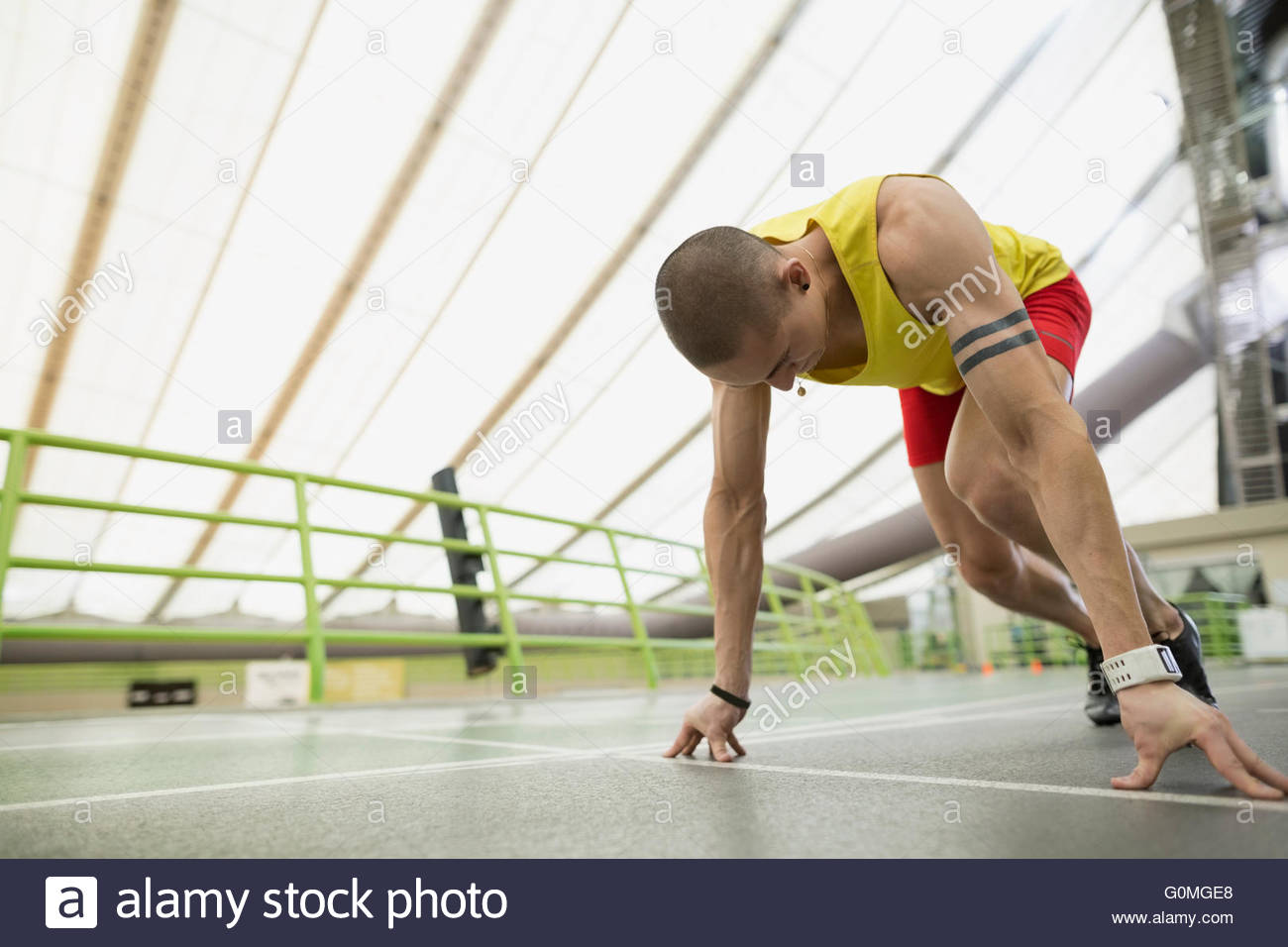 Runner poised at starting block on indoor track Stock Photo Alamy