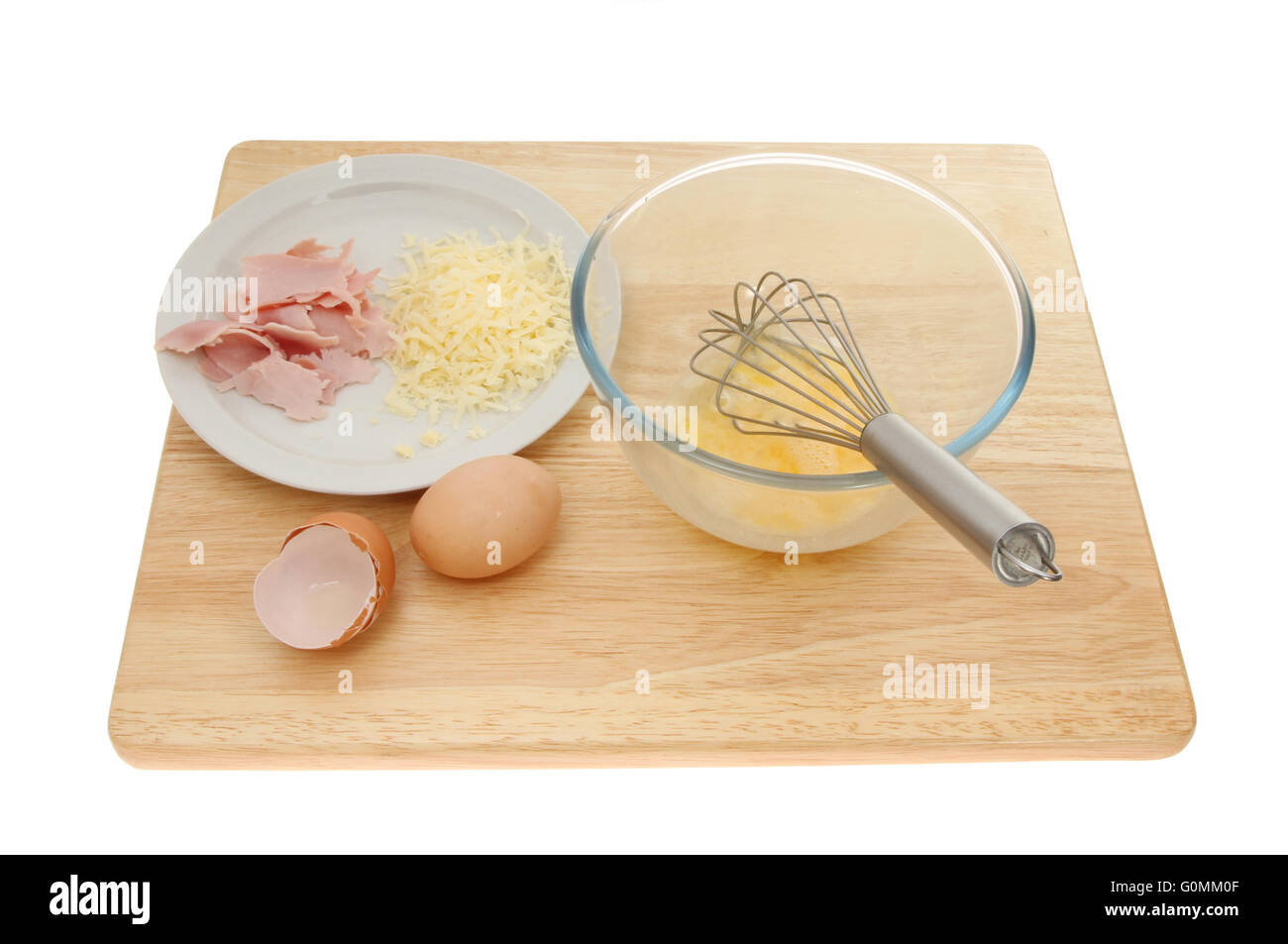 Omelette ingredients, eggs, cheese and ham with a whisk and mixing bowl on a wooden chopping board isolated against white Stock Photo