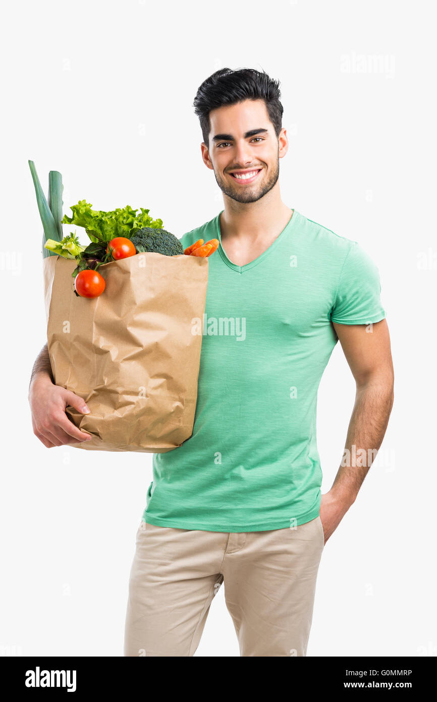 Handsome young man carrying a bag full of vegetables, isolated over gray background Stock Photo