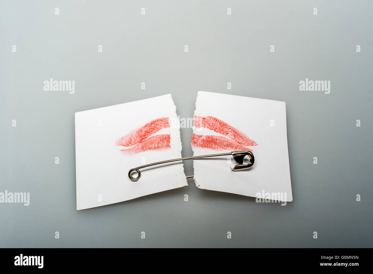 ripped visiting card  with red lip print connected with safety pin Stock Photo