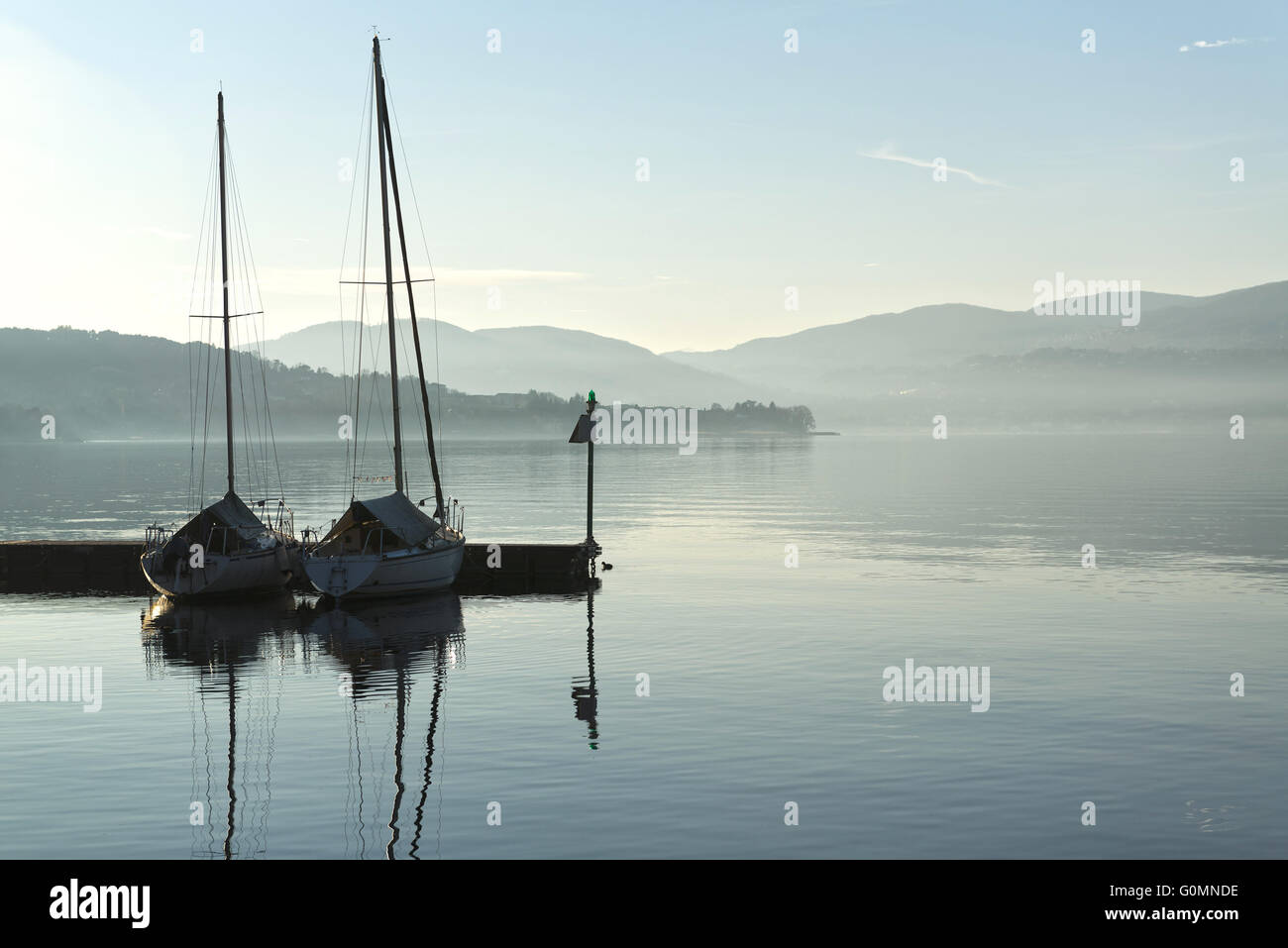 two boats in the harbor on a calm lake and the horizon mists of winter Stock Photo