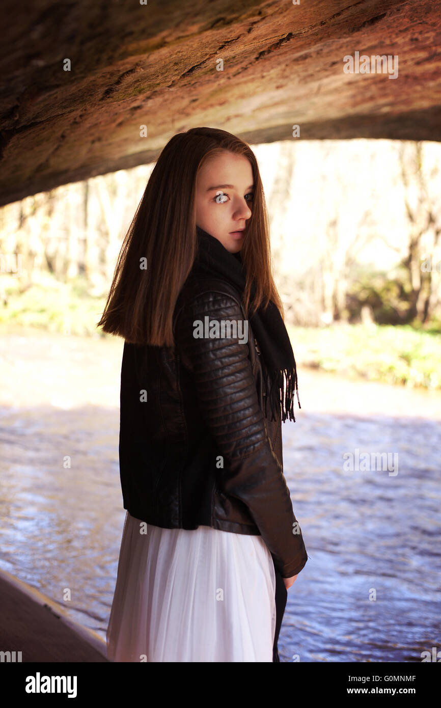 Beautiful teenage girl looking over her shoulder whilst standing under a bridge with a river in the background Stock Photo