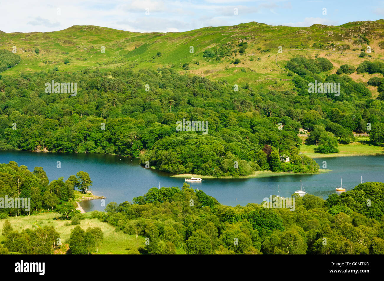 A launch passes the narrows of Coniston Water near Water Park. Bethecar Moor is on the skyline Stock Photo