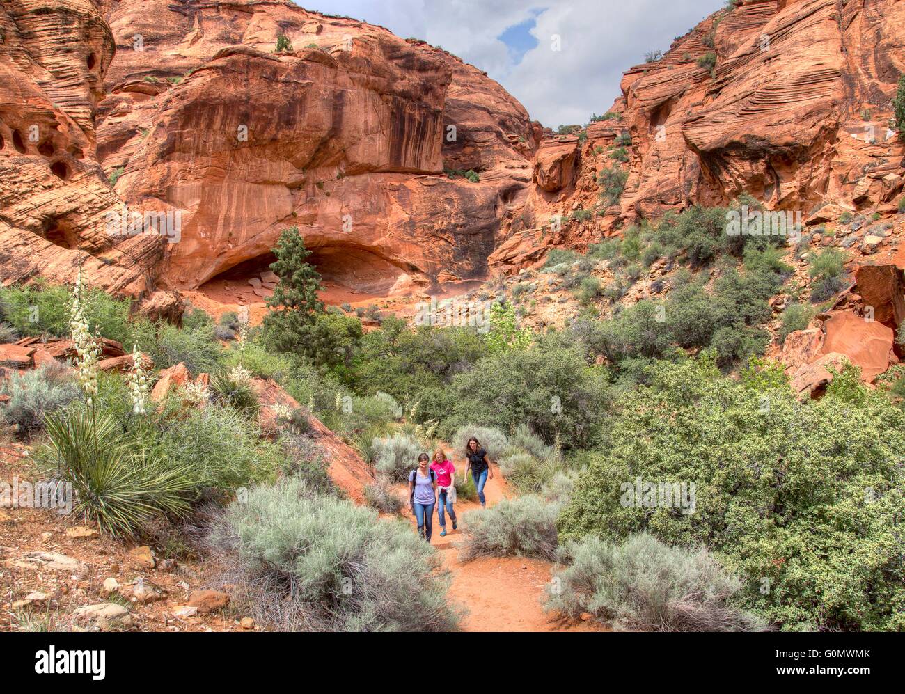 Hikers make their way through the rock hills and desert at the Red Cliffs National Conservation Area where the Colorado Plateau, Great Basin Desert, and Mojave Desert overlap near St. George, Utah. Stock Photo
