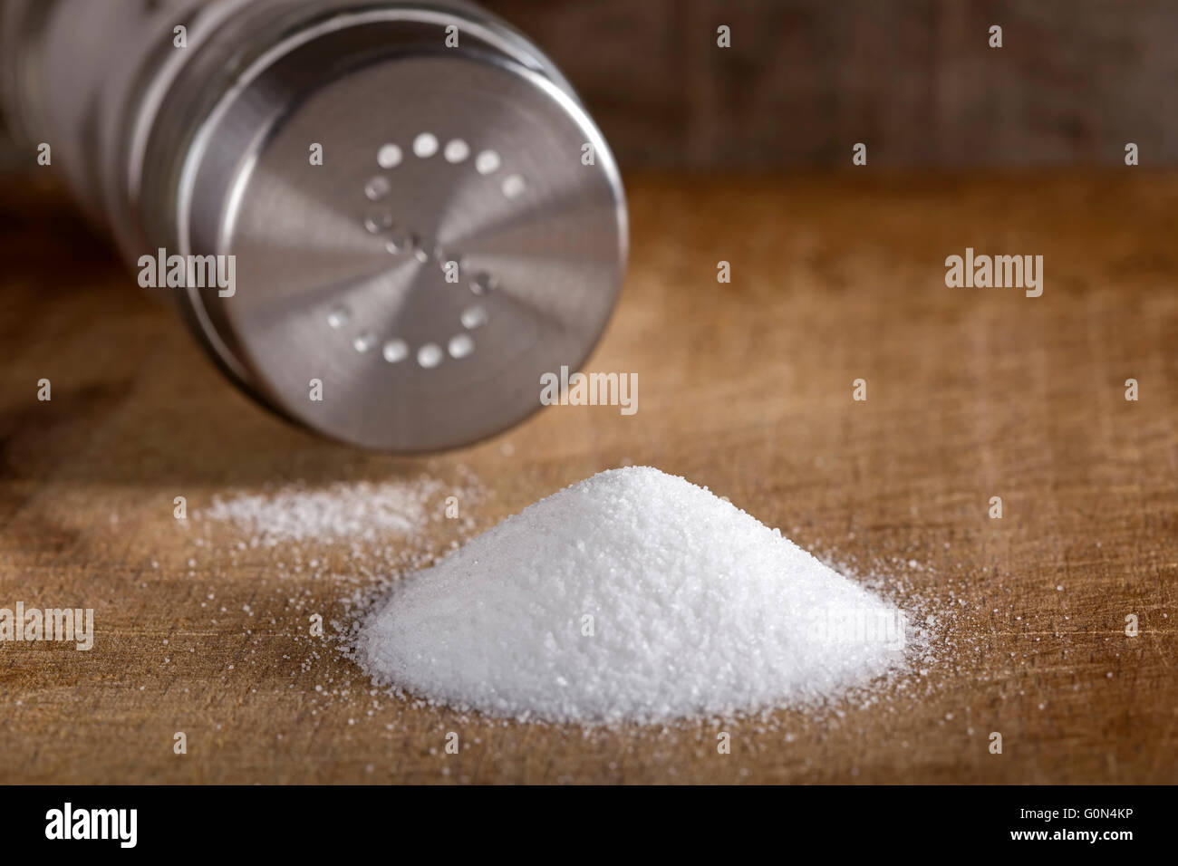 Salt spilling on wooden table from salt cellar Stock Photo