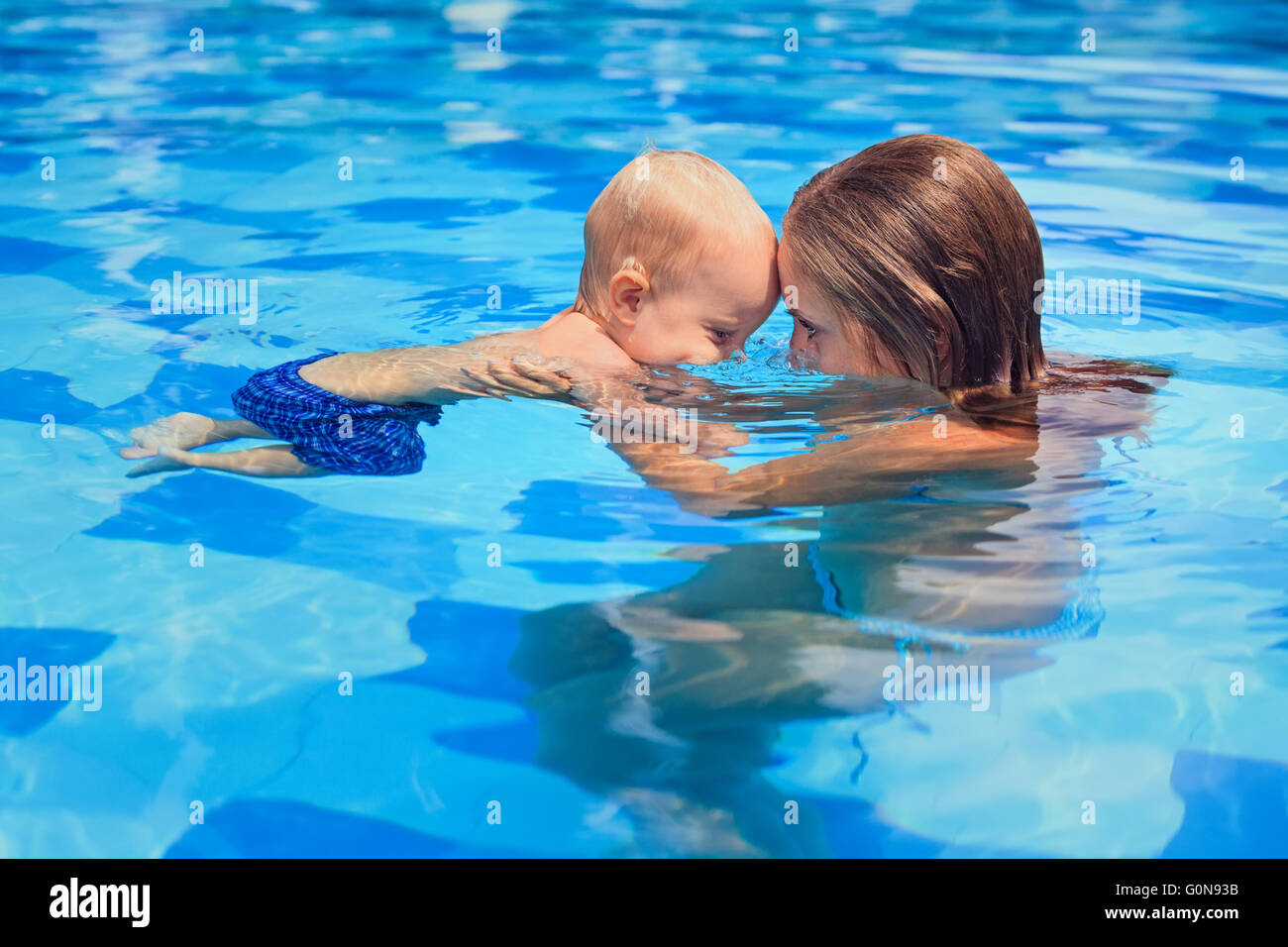 Happy little sports man with mother - active baby swim with fun in woman hands in swimming pool. Stock Photo