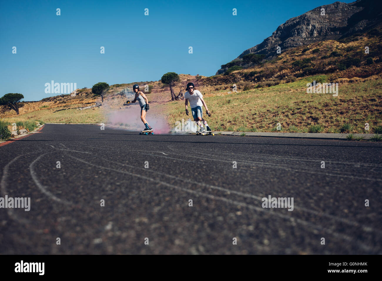Young man and woman skateboarding with smoke bomb on the road. Young couple practicing skating on a open road. Stock Photo