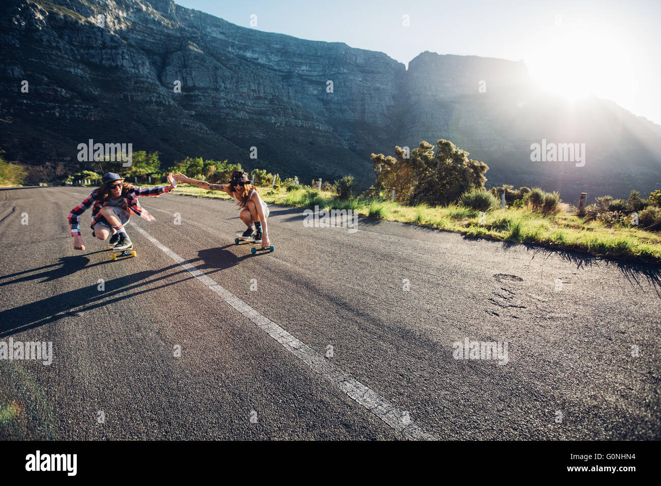 Young couple skating down on the road. Young man and woman having fun while skating together on a sunny day. Stock Photo
