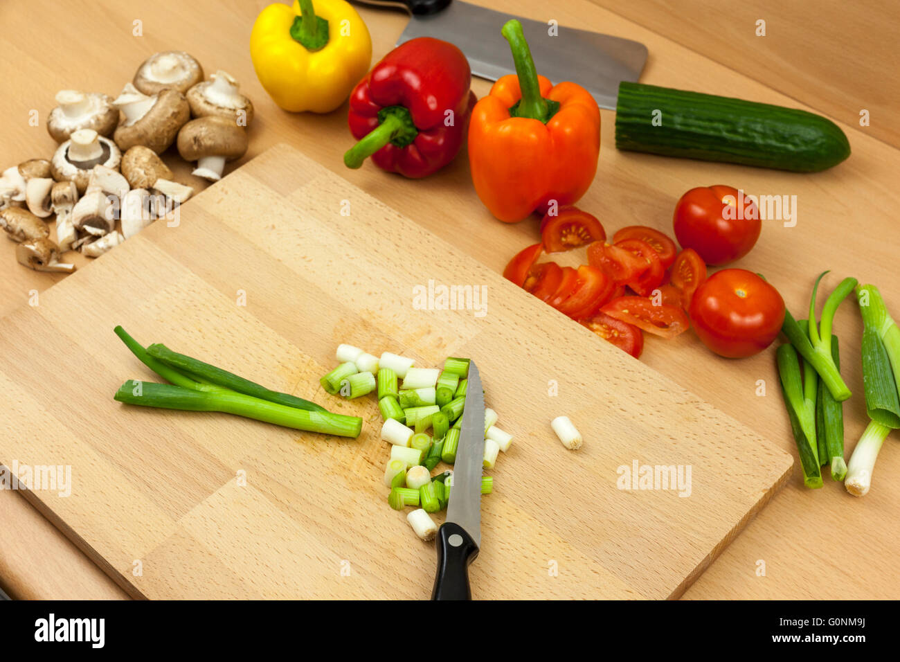 Knife laying on top of some freshly chopped salad onions on a chopping