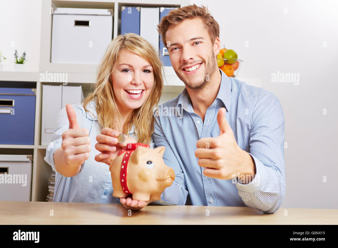 Smiling happy couple with piggy bank and monay holding their thumbs up ...