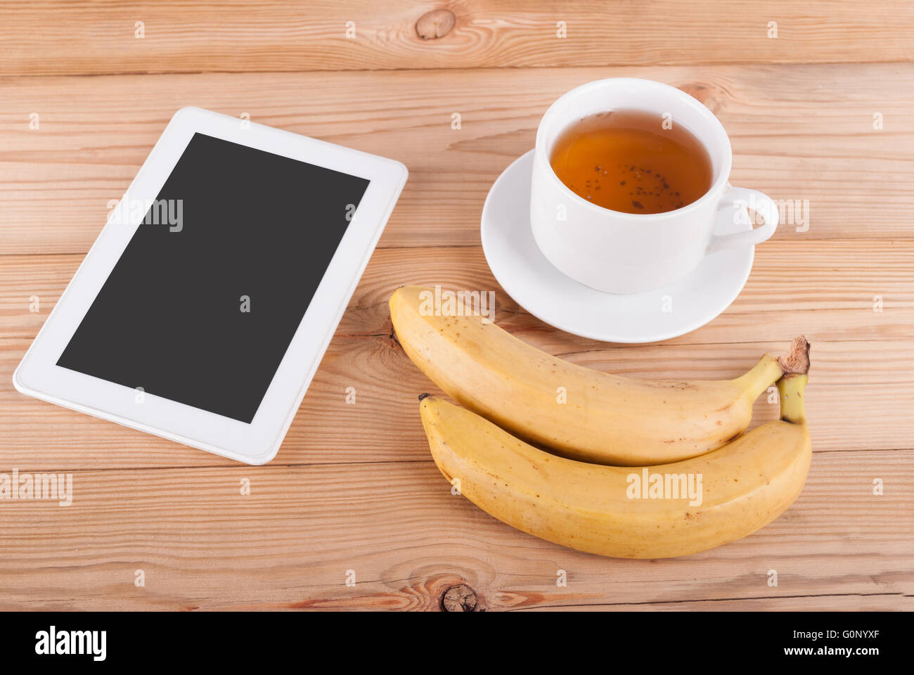Digital tablet cup of tea and bananas on a wooden table. Stock Photo