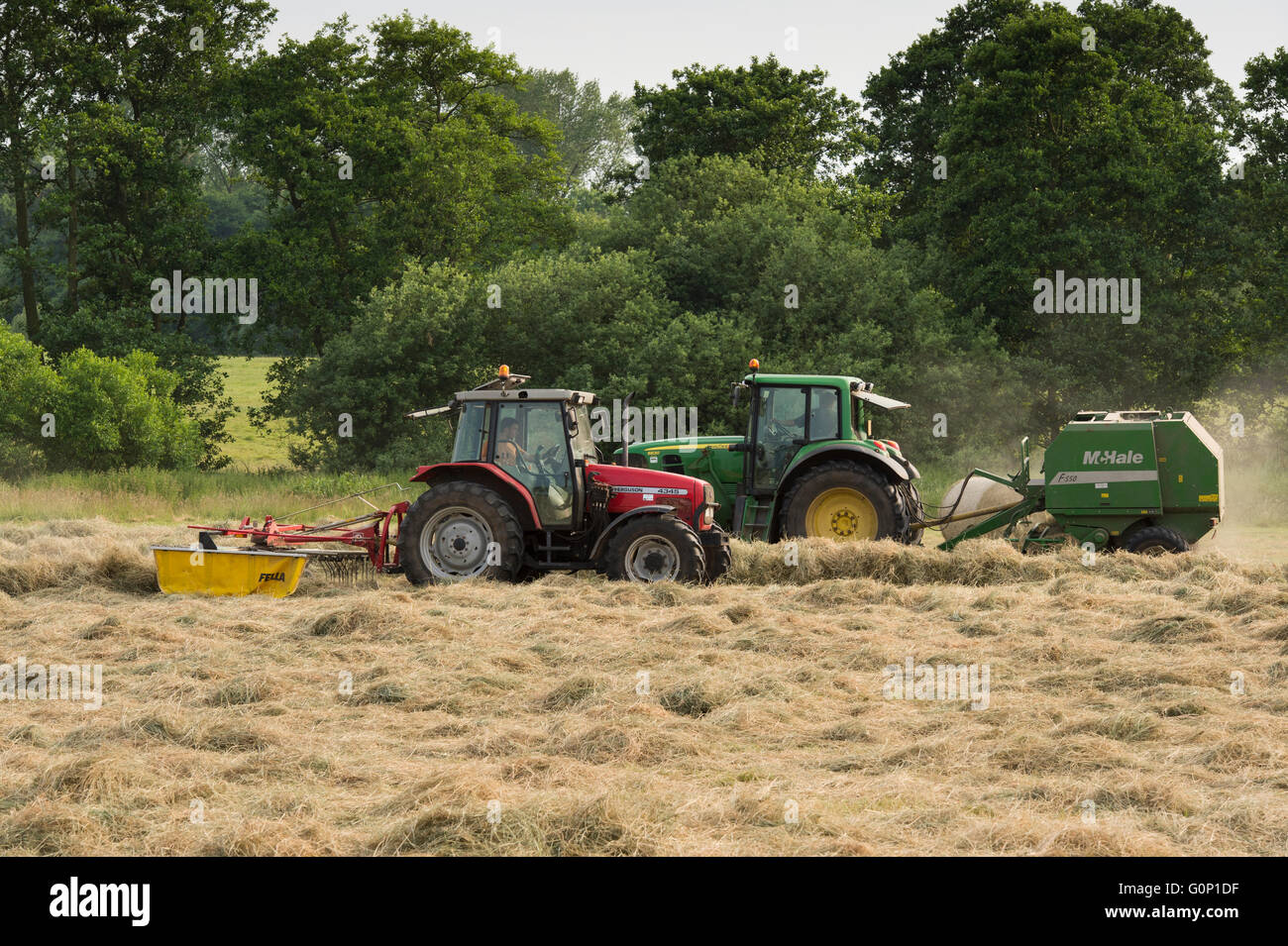 Two farm tractors silage making in a field at Great Ouseburn, North Yorkshire, England - a green one pulling a baler, a red one dragging a rake. Stock Photo