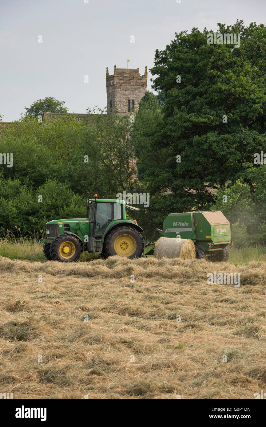 Silage or hay making - man is driving green farm tractor pulling a round baler, working in a field - Great Ouseburn, North Yorkshire, England, UK. Stock Photo