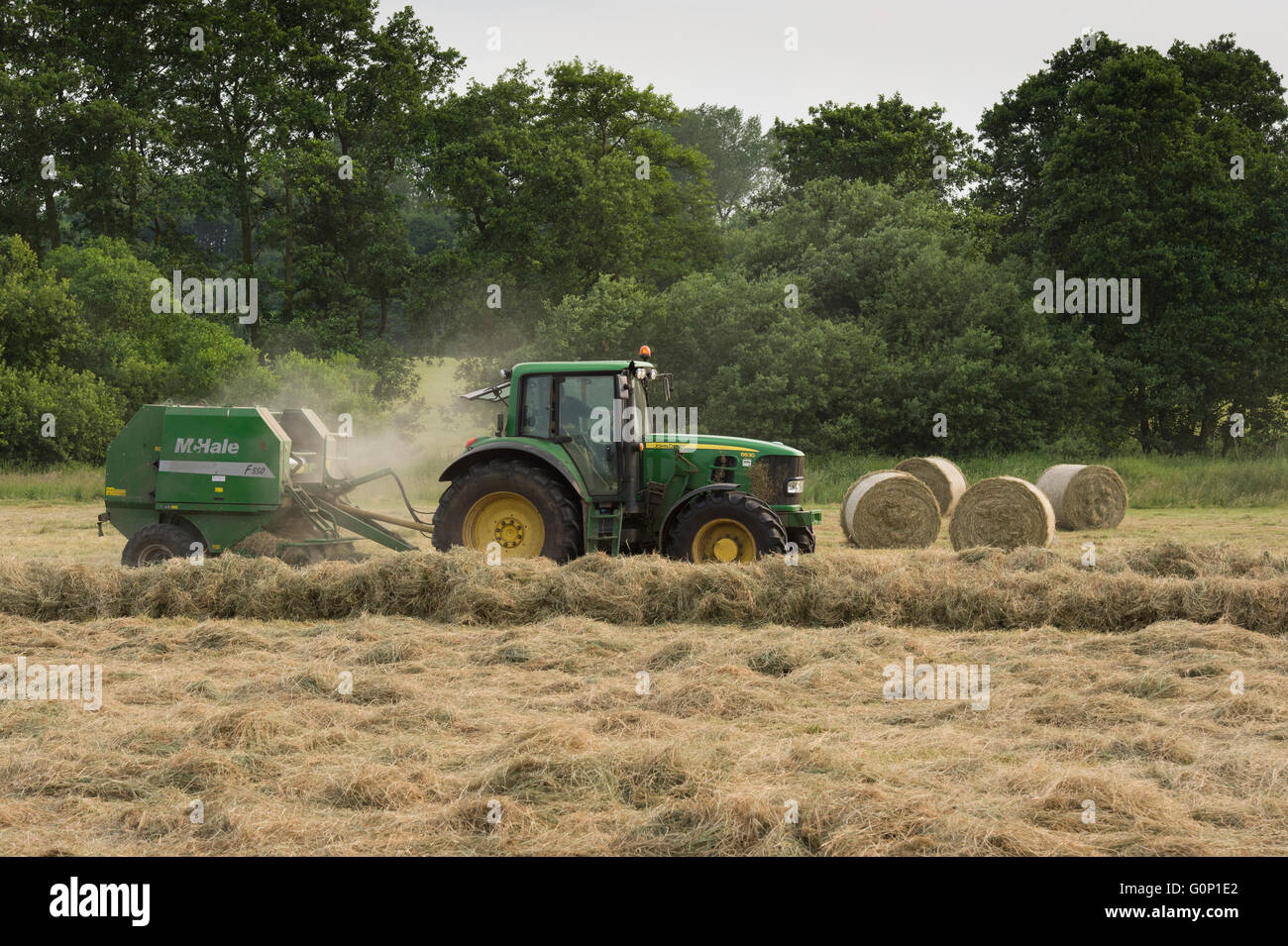 Farm tractor working in a field, silage making and pulling a round baler (4 bales beyond) - Great Ouseburn, North Yorkshire, GB. Stock Photo