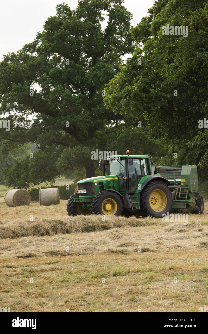 Hay or silage making, Great Ouseburn, North Yorkshire, England, UK - green farm tractor working in a field, pulling a baler with round bales beyond. Stock Photo