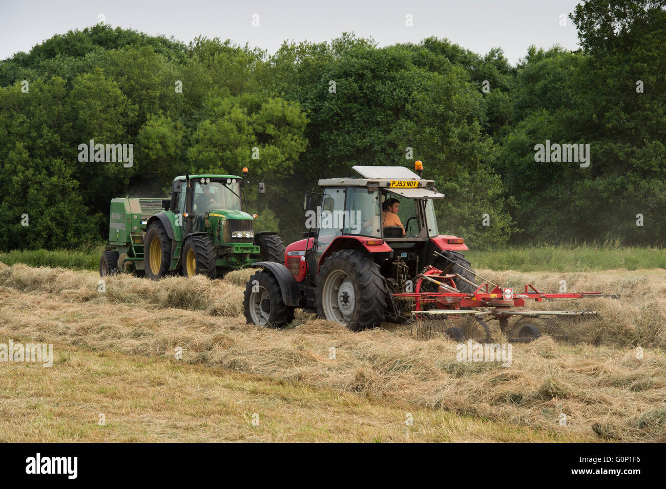 Two farm tractors silage making in a field at Great Ouseburn, North Yorkshire, England - the green one pulling a baler, the red one hauling a rake. Stock Photo